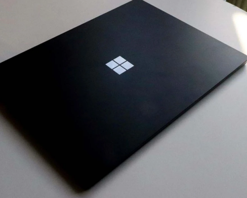 Image of a black laptop closed with windows logo on top, on top of a white desk