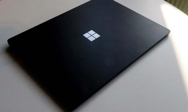 Image of a black laptop closed with windows logo on top, on top of a white desk